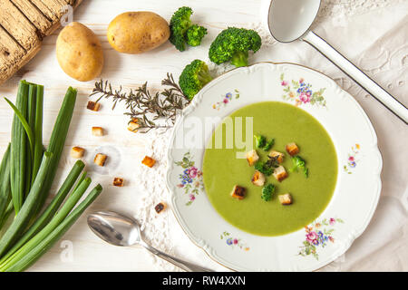 Frühling detox Brokkoli green Creme Suppe mit Kartoffeln und vegane Sahne in Schüssel auf hellen Holz- Platine mit weißem Hintergrund, Ansicht von oben. Sauber, Essen Stockfoto