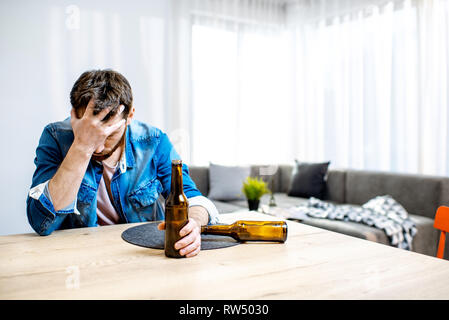 Betrunkene männliche Alkoholiker sitzen mit Flaschen deprimiert und leiden unter Kopfschmerzen zu Hause Stockfoto