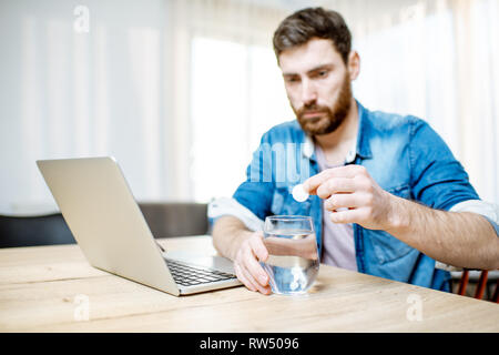 Mann, fiebersenkenden und schmerzlindernden Pillen schlechte Gefühl, während auf dem Laptop zu Hause arbeiten Stockfoto