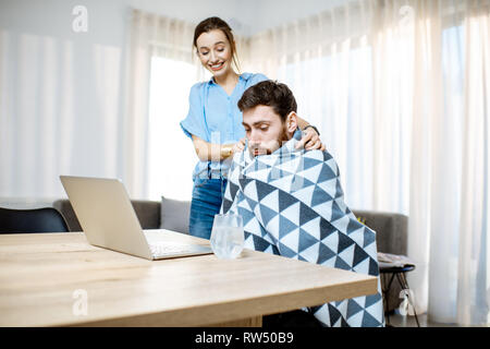 Junge Frau die Pflege geben etwas Medizin für einen Mann Krankheitsgefühl mit Decke zu Hause abgedeckt Stockfoto