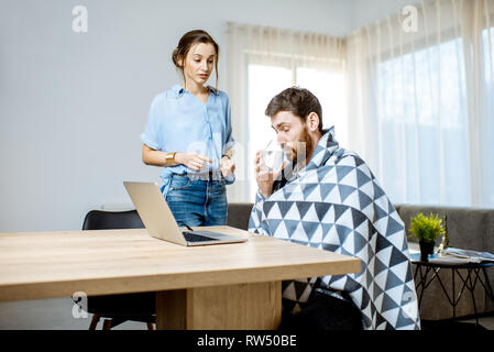 Junge Frau die Pflege geben etwas Medizin für einen Mann Krankheitsgefühl mit Decke zu Hause abgedeckt Stockfoto