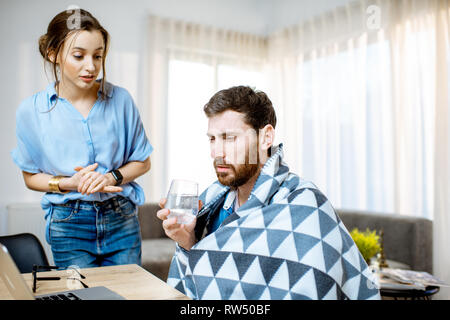Junge Frau die Pflege geben etwas Medizin für einen Mann Krankheitsgefühl mit Decke zu Hause abgedeckt Stockfoto