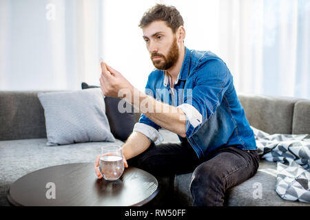 Mann trinken einige Arzneimittel schlechte Gefühl oder Kater nach der Alkohol Partei, sitzen auf der Couch zu Hause Stockfoto