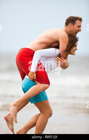 Junge Frau huckepack ihr Freund am Strand. Stockfoto