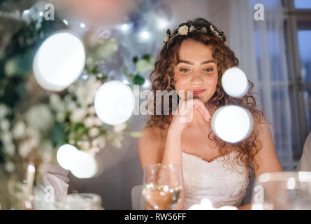 Die Vorderansicht des eine nachdenkliche junge Braut an einem Tisch auf einer Hochzeit sitzen. Kopieren Sie Platz. Stockfoto