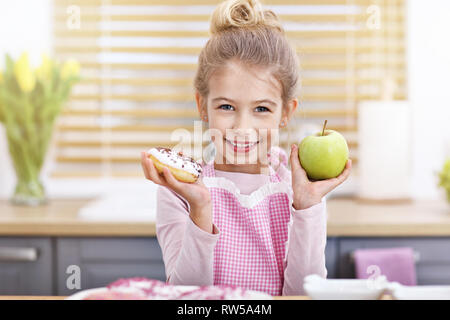 Süße kleine Mädchen die Wahl zwischen Apple und Donut in der Küche Stockfoto