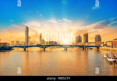 Schönen Sonnenuntergang über der City von London mit die Sonne: Sie erhellt die Gebäude und Battersea Bridge in England Stockfoto