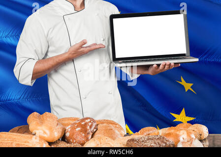 Baker holding Laptop auf der Fahne der Europäischen Union und Brot Hintergrund. Koch tragen einheitliche zeigt leeren Bildschirm zu kopieren. Stockfoto