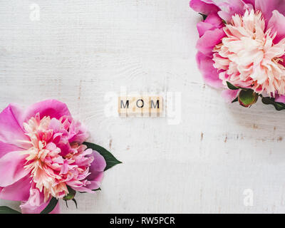 Bunte Pfingstrosen und Holz- Buchstaben des Alphabets in Form des Wortes isoliert Mama auf einem weißen Hintergrund. Ansicht von oben, close-up. Schöne Karte. Co Stockfoto