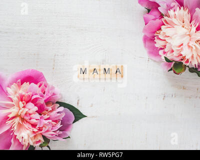 Bunte Pfingstrosen und Holz- Buchstaben des Alphabets in Form des Wortes isoliert Mama auf einem weißen Hintergrund. Ansicht von oben, close-up. Schöne Karte. Co Stockfoto