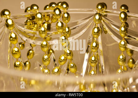 Makro Zusammenfassung von Gold Farbe Mardi Gras Perlen drapiert über wunderschöne Kristallglas Stockfoto