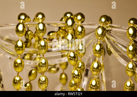 Makro Zusammenfassung von Gold Farbe Mardi Gras Perlen drapiert über wunderschöne Kristallglas Stockfoto