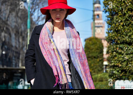 Fashion model pose mit einem roten har, Schal und schwarzen Mantel für ein Portrait mit Castelo Sforzesco in Mailand im Hintergrund an einem sonnigen Tag Stockfoto