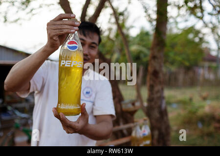 Ein Anbieter, der Kraftstoff für Motorräder mit Flaschen aus einem Fass gefüllt. Benzin ist in das Fahrrad aus der Flasche gegossen. Kampot, Kambodscha Stockfoto