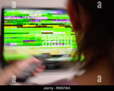 Ansicht der Rückseite Frau holding Fernbedienung auf schlechtes Signal statische Geräusche aus Ihren digitalen DTV Fernseher Flachbildschirm Swirl-effekt suchen Stockfoto