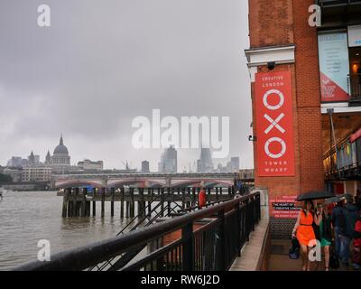 Zwei Damen, die für eine Nacht in London Pass durch die OXO Tower gekleidet am Südufer der Themse, holding Sonnenschirme gegen den Regen. Stockfoto