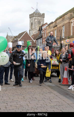 Salisbury, Wiltshire, UK. 5 Mär, 2019. Wettbewerber in den jährlichen Pfannkuchen Rennen an der High Street, Salisbury konkurrieren. Die Veranstaltung wird von St. Thomas Kirche und die trussell Trust organisiert. Stockfoto