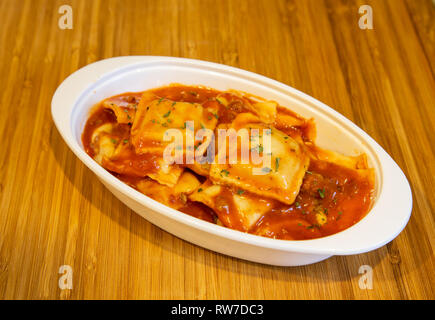 Frische Ravioli in Tomatensauce in einem weißen Teller auf einem Holz Schneidebrett zubereitet. Stockfoto