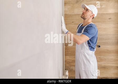 Keramische Fliesen Wand Endbearbeitung. Kaukasische Fliesen Installer Kontrolle auf der fertigen Wand im Badezimmer. Stockfoto