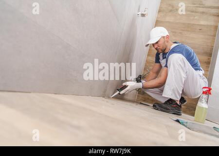 Kaukasische Arbeiter in seinem 30s Abdichtung der Wand Ecken von keramischen Fliesen im neu renovierten Bad. Mit Silikondichtmittel. Stockfoto