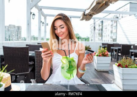 Schöne Frau Sommer Cafe, sitzend Table Restaurant. Glücklich lächelnde Ruhe nach der Arbeit das Mittag- oder Abendessen. Zahlt Kunststoff Kreditkarte, Anwendung, online Stockfoto