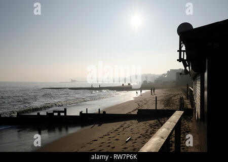 Eine Gruppe von Freunden zu Fuß entlang Sandown Strand in Silhouette, im hellen Sonnenschein dunstig. Stockfoto