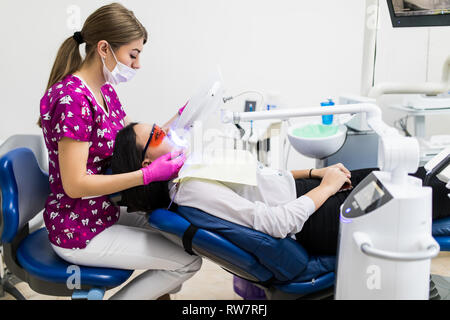 Close-up Portrait einer Patientin beim Zahnarzt in der Klinik. Zahnweiß-Verfahren mit UV-Licht UV Lampe. Stockfoto