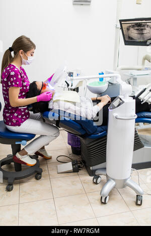 Close-up Portrait einer Patientin beim Zahnarzt in der Klinik. Zahnweiß-Verfahren mit UV-Licht UV Lampe. Stockfoto