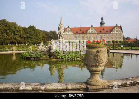 Rote Blumen in der Pflanzmaschine und Brunnen mit Statue im Schloss Weikersheim Garten im Spätsommer, Hohenlohe, Deutschland Stockfoto