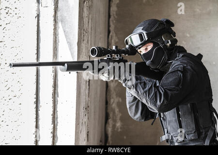 SWAT Polizei Operator mit Scharfschützengewehr mit dem Ziel, aus dem Fenster. Stockfoto