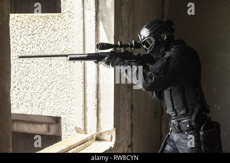 SWAT Polizei Operator mit Scharfschützengewehr mit dem Ziel, aus dem Fenster. Stockfoto