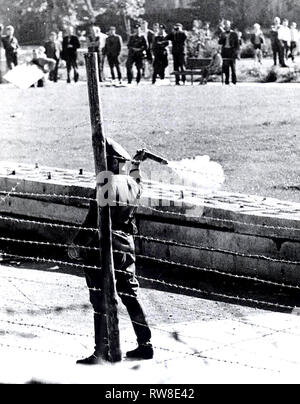 Oktober 1961-kommunistischen "Polizisten" (volkspolizist), stehen zwischen den Grenzzaun und Wand, bereitet eine Tear-Gas Granate bei einer Gruppe von West-berliner, die auf Ihrer Seite der Grenze versammelt die Roten Garden zu Jeer zu werfen Stockfoto