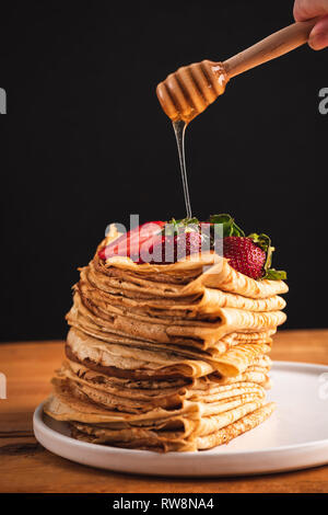 Gießen Honig über Stapel von Blini, Crepes, dünne Pfannkuchen. Auf schwarzen Hintergrund mit Kopie Platz für Text. Leckeres Frühstück essen, Dessert, traditionelle Rus Stockfoto