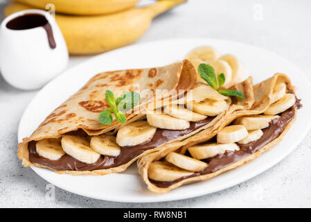 Crepes gefüllt mit Schokolade und Banane auf weiße Platte. Dünne Pfannkuchen, Blini. Süße Nachspeise. Stockfoto