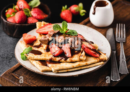 Französische Crêpes mit Schokoladensauce und Erdbeeren auf Platte auf Holz, das Board Stockfoto