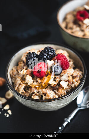 Schüssel Haferbrei Porridge mit Nüssen und Beeren auf schwarzem Hintergrund. Gesunde vegane oder vegetarische Kost Stockfoto