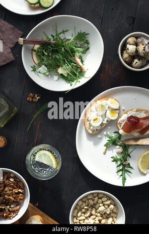 Gesundes Mittagessen auf dunklem Hintergrund der Ansicht von oben. Verschiedene Sandwiches und Rucola Salat zum Frühstück, Vorspeisen, Snacks Stockfoto