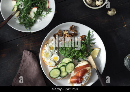 Verschiedene Sandwiches und Rucola Salat zum Frühstück, Vorspeisen, Snacks. Gesundes Mittagessen auf dunklen Holztisch, Ansicht von oben Stockfoto