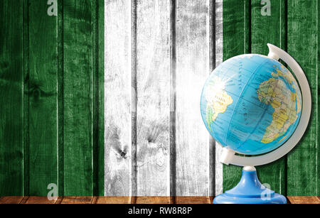 Globus mit einer Weltkarte auf einem hölzernen Hintergrund mit dem Bild der Flagge von Nigeria. Das Konzept der Reisen und Freizeit im Ausland. Stockfoto