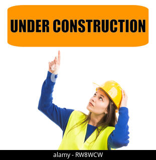 Junge weibliche Bauarbeiter zeigt mit dem Zeigefinger auf Im Bau Zeichen über dem Kopf halten gelb Sicherheit hardhat Stockfoto