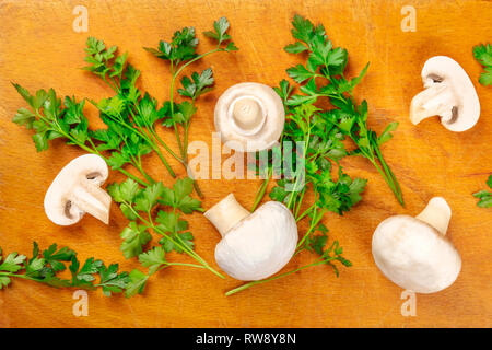 Champignons, ganz und geschnitten, Schuß von oben auf eine rustikale Schneidbrett mit frischer Petersilie Stockfoto