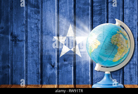 Globus mit einer Weltkarte auf einem hölzernen Hintergrund mit dem Bild der Flagge Somalias. Das Konzept der Reisen und Freizeit im Ausland. Stockfoto