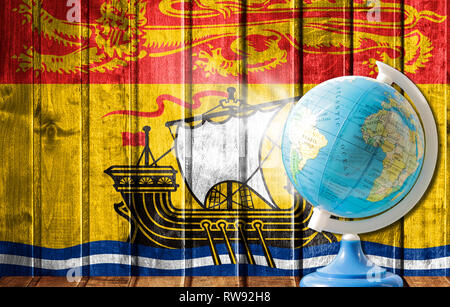 Globus mit einer Weltkarte auf einem hölzernen Hintergrund mit dem Bild der Flagge von New Brunswick. Das Konzept der Reisen und Freizeit im Ausland. Stockfoto