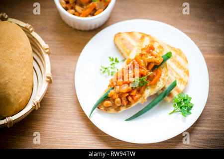 Gebratenes Brot Toast mit geschmorte Bohnen und Gemüse in einer Platte auf einem Holztisch Stockfoto