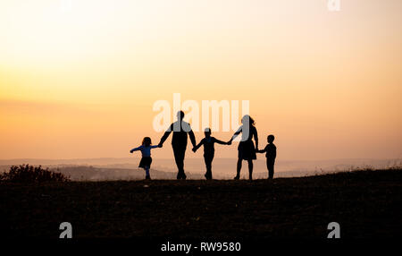 Silhouetten der glückliche Familie an der Hand in die Wiese während des Sonnenuntergangs. Stockfoto