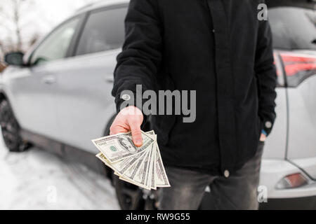 Mann mit Geld in der Nähe von Autos. Geld Dollar in den Kraftstofftank. Stockfoto