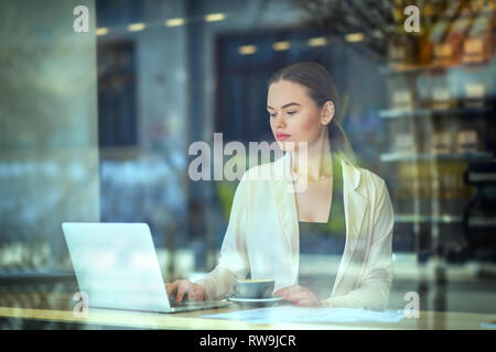 Junge Frau am Fenster sitzen im Cafe Kaffee trinken während der Arbeit am Computer Stockfoto