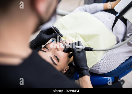 Junge attraktive erfolgreiche Zahnarzt in Zahnarztpraxis Instandsetzung Zähne von jungen weiblichen Patienten in den zahnmedizinischen Stuhl sitzen. Stockfoto