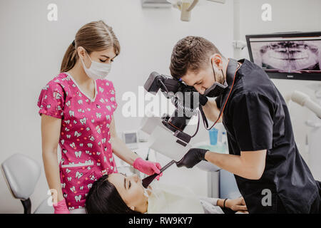 Der junge Mann Zahnarzt die Zähne der weiblichen Patienten in der Zahnarztpraxis. Stockfoto