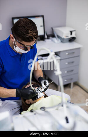 Mann an Zahnarzt Klinik erhält der zahnmedizinischen Behandlung ein Loch in einen Zahn zu füllen. Zahnersatz und Verbundmaterial Polymerisation Behandlung der Zähne. Stockfoto